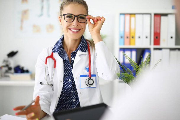 Mujer doctora con gafas sonriendo en el lugar de trabajo en consultorio médico - Foto, Imagen