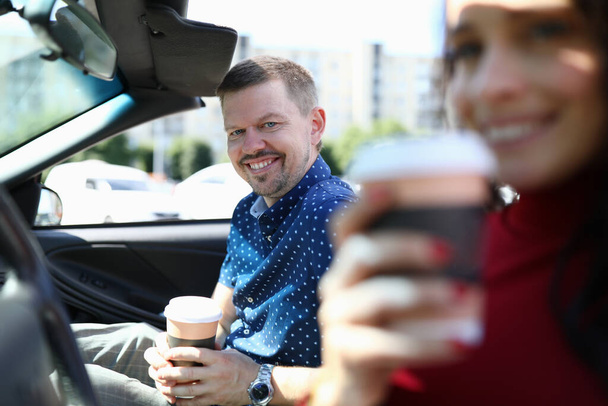 Man and woman are sitting in car smiling and drinking coffee - Foto, Imagem