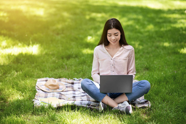 Koreaanse student meisje studeren buiten met laptop in het park, zittend op het gazon - Foto, afbeelding
