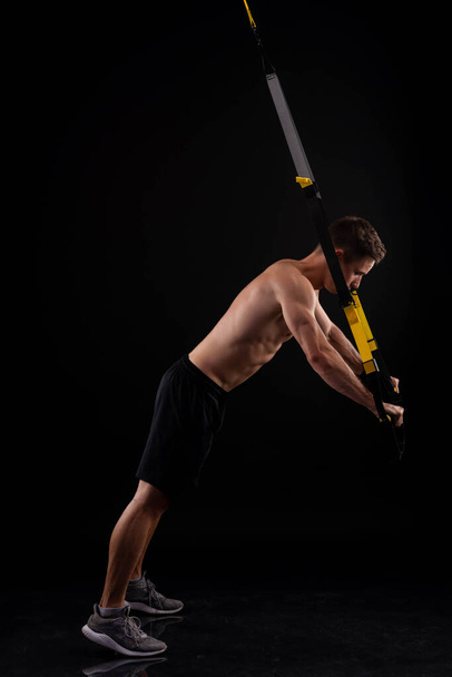 Athletic muscular man doing exercises on trx loops. Body-building. Active lifestyle. - Photo, image