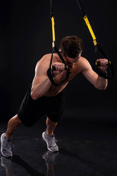 Athletic muscular man doing exercises on trx loops. Body-building. Active lifestyle. - Foto, Imagem