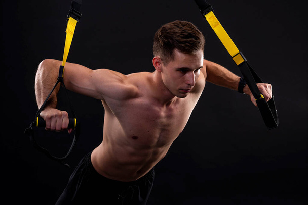 Athletic muscular man doing exercises on trx loops. Body-building. Active lifestyle. - Foto, Bild