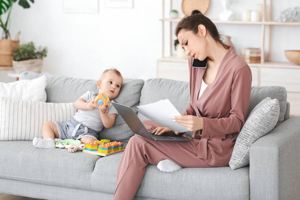 Mère travaillant à la maison avec un ordinateur portable et des papiers à côté de son bébé - Photo, image