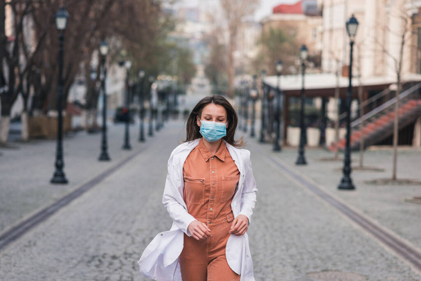 egy narancssárga ruhás barna nő fehér orvosi kabátban és védőmaszkkal az arcán. - Fotó, kép