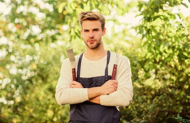 Picnic concept. Bbq chef. Handsome guy cooking food. Grilling food. Barbecue utensils. Cooking burgers. Man hold barbeque equipment. Summer weekend. Tools for roasting meat outdoors. Barbeque party - Fotoğraf, Görsel