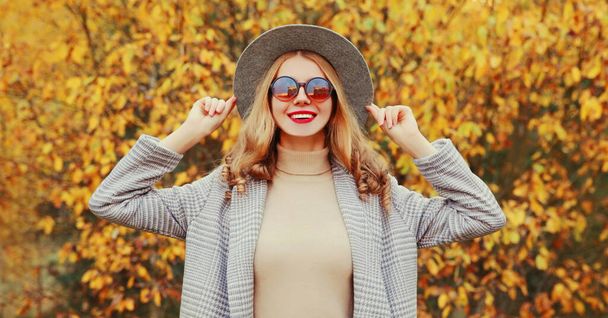 Autumn portrait of beautiful young woman wearing gray coat, round hat posing over yellow leaves background - Fotografie, Obrázek