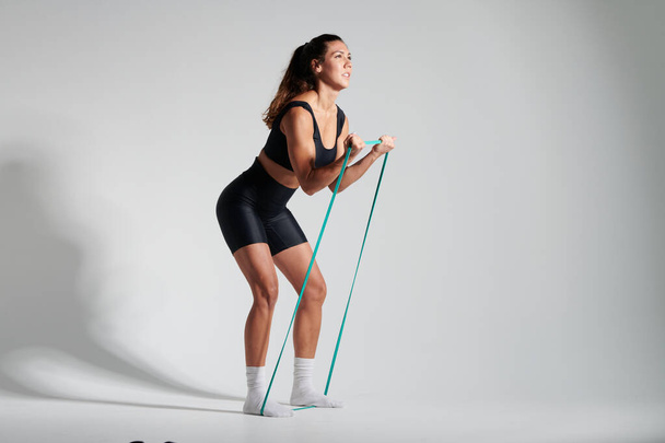 фитнес-девушка в черном натягивает резину - Фото, изображение