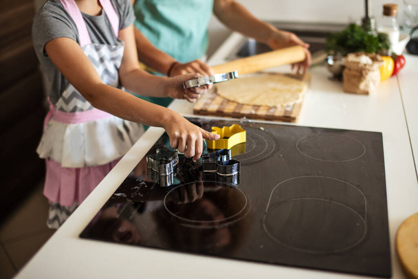Child and women cutting form for cookie in dough. Happy family and childhood. - 写真・画像