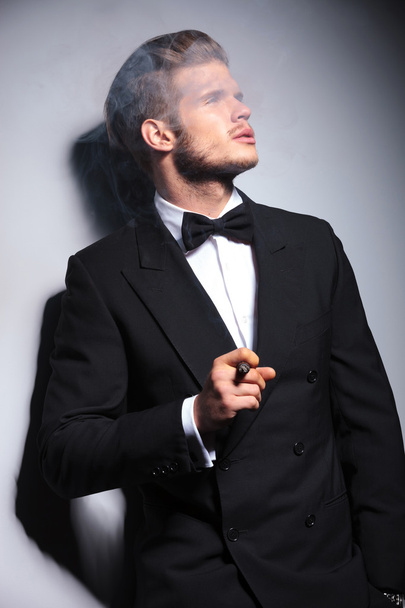 fashion man in tuxedo and bow tie blowing his smoke - Foto, afbeelding