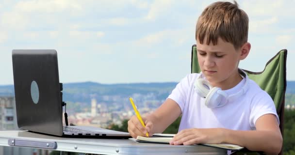 o menino escreve dados em um caderno, coloca fones de ouvido e trabalha em um laptop
 - Filmagem, Vídeo