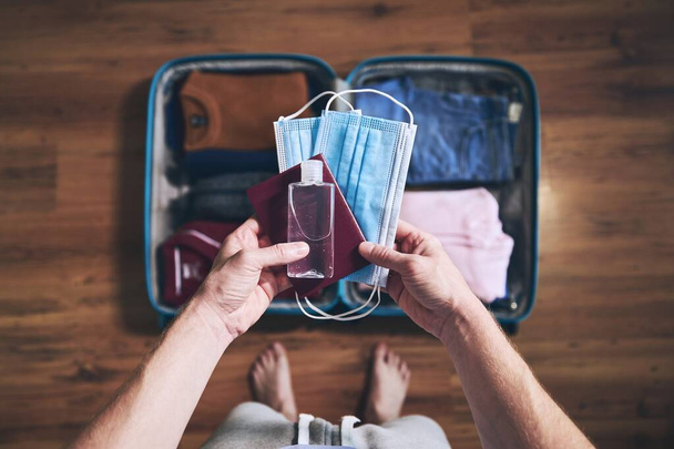 Preparing for travel in new normal. Man packing passport, face masks and hand sanitizer. Themes personal protection and flight rules during coronavirus pandemic. - Foto, immagini