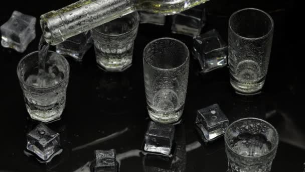 Barman giet bevroren wodka uit fles in borrelglas. IJsblokjes tegen donkere natte zwarte achtergrond - Video