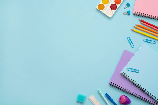 Colorful stationery set on blue background. Top view of blue, pink and purple notebooks, paper pins, eraser, felt tip pens, color pencils and watercolor. Back to school. Copy space.  - Φωτογραφία, εικόνα