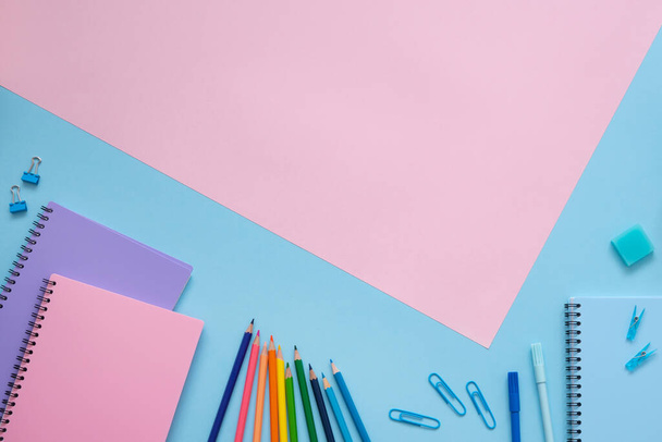 Education concept. Blue, purple and pink notebooks, color pencils, felt tip pens, eraser and paper clips on the background and copy space on pink background. Top view. - Fotografie, Obrázek