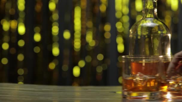Barman empuja, pone dos vasos con whisky dorado, coñac o brandy con cubitos de hielo en la mesa de madera - Metraje, vídeo