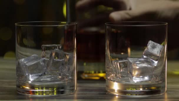 Verter el whisky, el coñac o el brandy de la botella en vasos con hielo. Fondo brillante - Metraje, vídeo