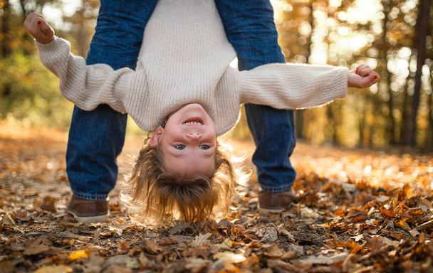 Unrecognizable father holding small daughter upside down in autumn forest. - Fotografie, Obrázek