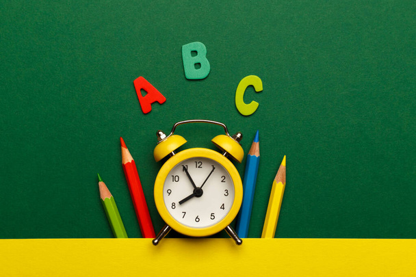 Concepto de regreso a la escuela, con letras de madera coloridas y reloj despertador amarillo sobre fondo de madera verde - Foto, Imagen
