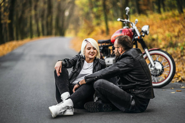 Досить пара сидить біля червоного мотоцикла на дорозі в лісі з барвистим вороненим тлом. Концепція відносин
. - Фото, зображення