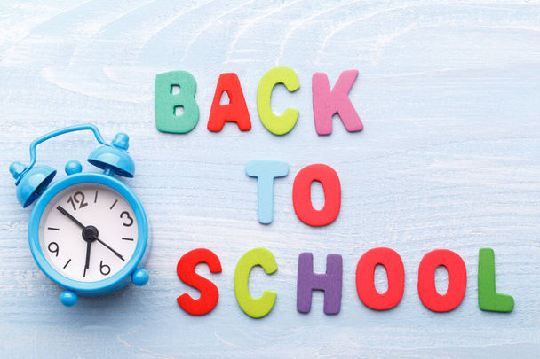 Concepto de regreso a la escuela, con letras de madera coloridas y reloj despertador sobre fondo de madera azul
 - Foto, imagen