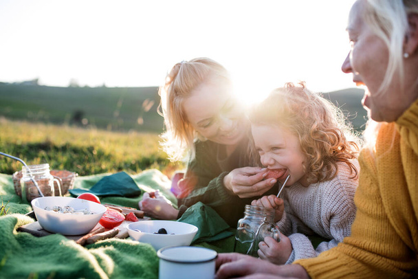 Small girl with mother and grandmother having picnic in nature at sunset. - Φωτογραφία, εικόνα