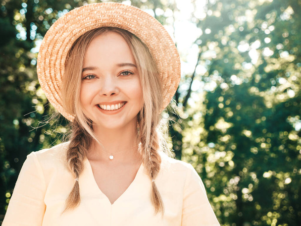 Portrait of young beautiful smiling hipster girl in trendy summer sundress. Sexy carefree woman posing on the street background in the park in hat at sunset. Positive model outdoors - Foto, Bild