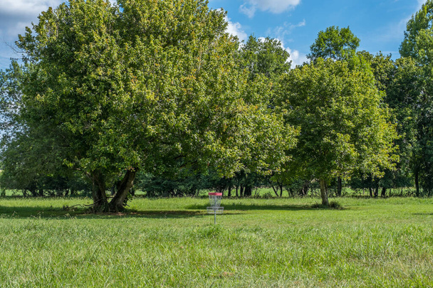 An empty disc golf basket in the open field with the woodlands in the background on a bright day in summertime - Фото, зображення