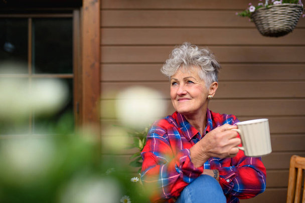 Senior woman with coffee sitting on terrace in summer, resting. - Fotografie, Obrázek