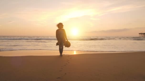 Mulher relaxada andando na praia se aproximando da água do mar câmera lenta fugindo da onda de espuma
 - Filmagem, Vídeo