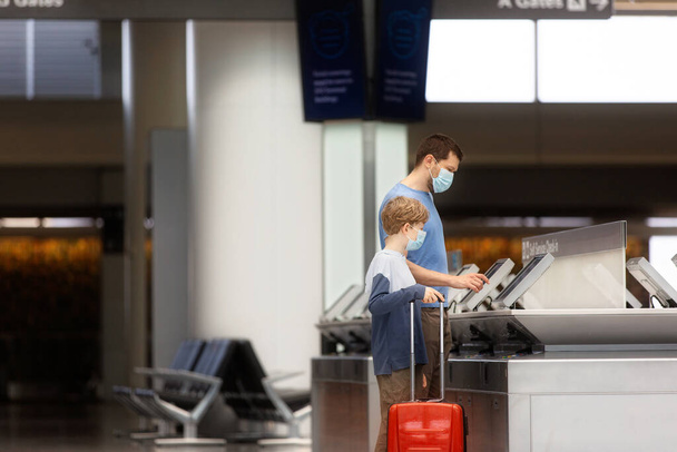 family of two, father and son, in face masks standing with the luggage in the airport, travel during coronavirus pandemic concept - Zdjęcie, obraz