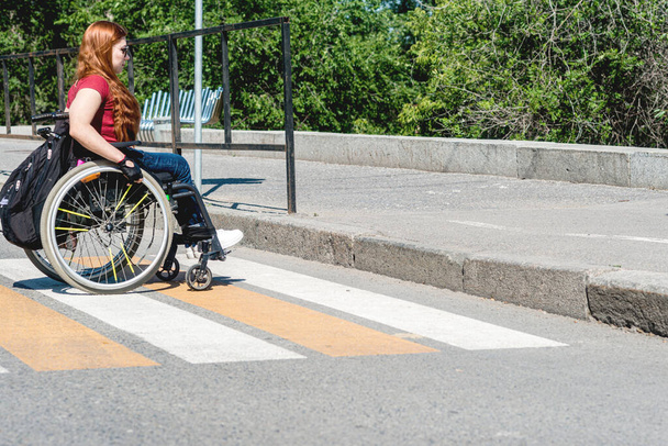 横断歩道で高い縁石の前の車椅子の若い女性。障害者のための低移動性の概念. - 写真・画像