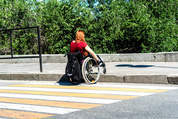 Młoda kobieta na wózku inwalidzkim przed wysokim krawężnikiem przy przejściu dla pieszych. Koncepcja niskiej mobilności osób niepełnosprawnych. - Zdjęcie, obraz