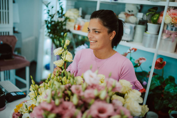 Retrato de una joven hermosa florista caucásica en un vestido rosa que arregla un ramo de flores en una florería - Foto, Imagen