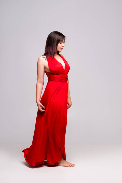 Beautiful woman in red dress in studio on gray background, full-length portrait - 写真・画像