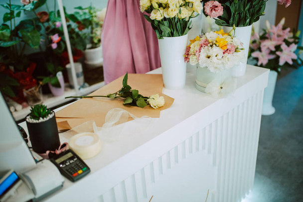Κλείσιμο τραπεζιού στο οποίο ένα μπουκέτο φρέσκα λουλούδια είναι τοποθετημένα σε ανθοπωλείο. Τριαντάφυλλα σε ανθοπωλείο - Φωτογραφία, εικόνα