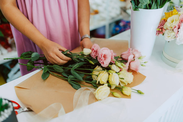 Zbliżenie rąk białej kobiety w różowej sukience układającej bukiet kwiatów na stole w kwiaciarni. Robiąc bukiet kwiatów - Zdjęcie, obraz