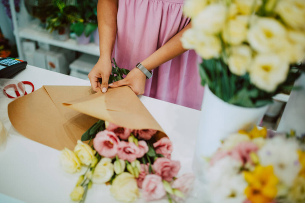 Closeup of hands of a caucasian woman in a pink dress arranging a bouquet of flowers on a table in a flower shop. Making a bouquet of flowers - Фото, изображение