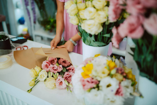 Closeup of hands of a caucasian woman in a pink dress arranging a bouquet of flowers on a table in a flower shop. Making a bouquet of flowers - Фото, изображение