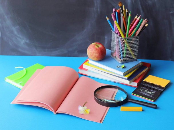 Terug naar school, briefpapier, vergrootglas, stapel boeken, appel op tafel, home learning concept, onderdeel van kinderkamer interieur - Foto, afbeelding