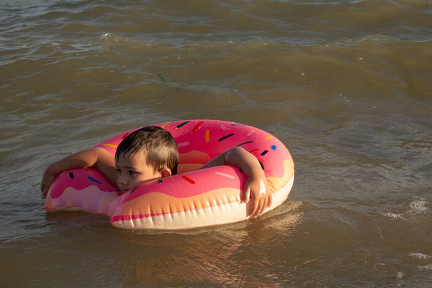 晴れた日にドーナツの形で膨脹可能なリング上の海で陽気な少年5歳の水泳 - 写真・画像