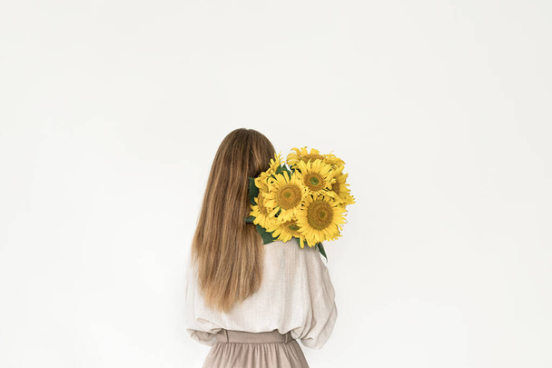 Beautiful young woman in linen dress holding sunflowers bouquet. - Photo, image