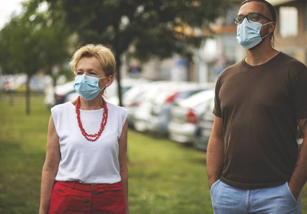 Blonde Woman and her son Wearing a Mask.Social distancing. Senior woman and young man, during Covid-19 pandemic, outdoor. - Foto, afbeelding