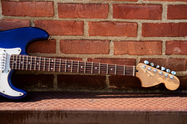 Modrá elektrická kytara proti cihlové zdi mimo hudební scénu - Fotografie, Obrázek
