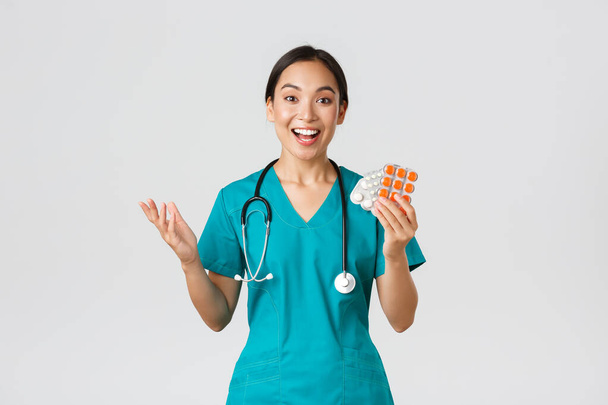 Sağlık çalışanları, virüsü önleme, karantina kampanyası konsepti. Heyecanlı mutlu Asyalı kadın doktor, tıbbi maske takan hemşire harika yeni ilaçlar gösteriyor, eczane tavsiye ediyorlar. - Fotoğraf, Görsel