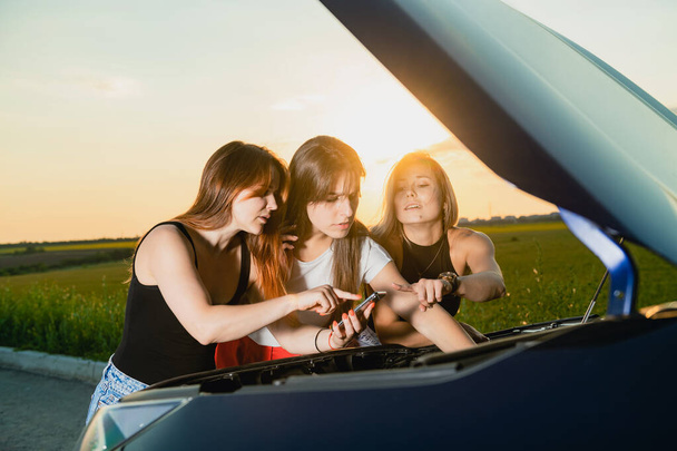 車のエンジンを修復しようとしている間に情報を検索する3人の女の子. - 写真・画像