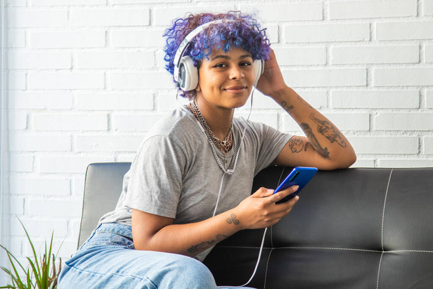 молодая афроамериканка слушает музыку по телефону на диване - Фото, изображение