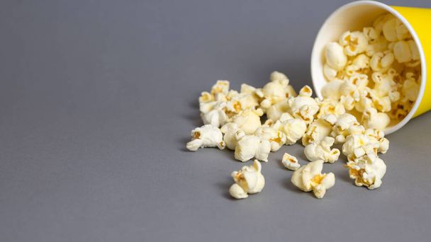 Popcorn in a yellow paper cup on grey background. Copy space - Photo, Image