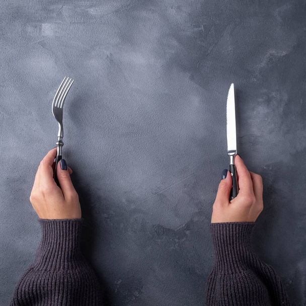 Mani che tengono forchetta e coltello su sfondo grigio. Vista dall'alto con spazio di copia - Foto, immagini
