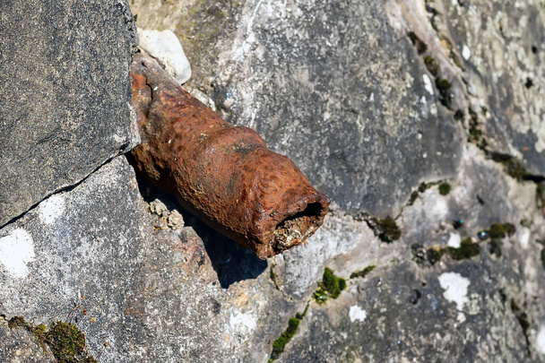 An old rusty pipe sticks out of a stone wall. The tube looks like an old sore penis. Impotence, genital diseases in men concept. - Zdjęcie, obraz