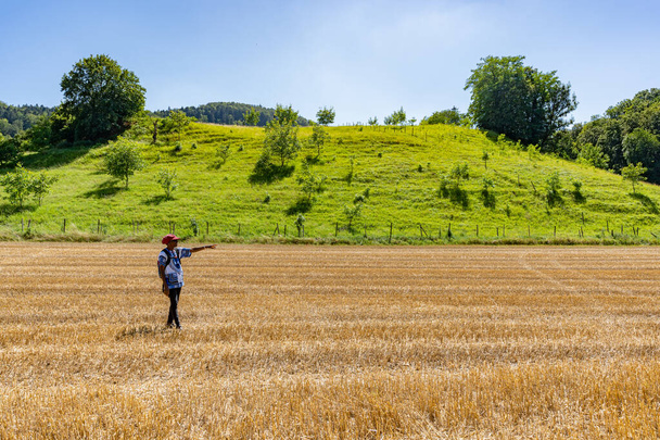 Zwarte vrouw staat in gouden veld met rode hoed op heldere zonnige dag. Reizigersvrouw op geoogst maïsveld in Linn Boezberg, Zwitserland. - Foto, afbeelding